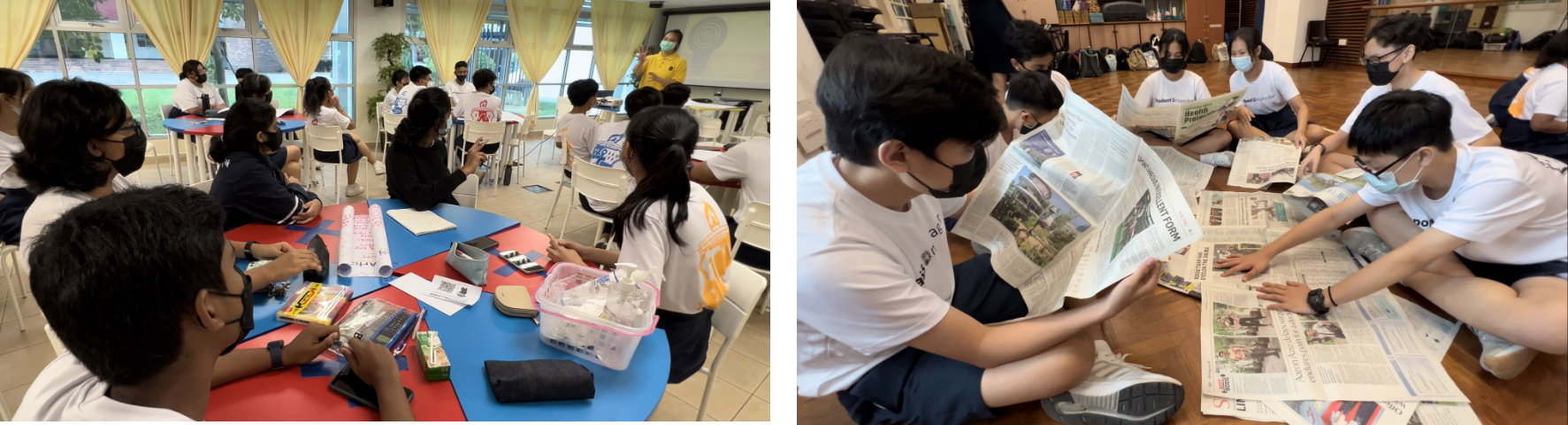 Students wearing masks sit at tables in a classroom and read newspapers spread on the floor in a hall.